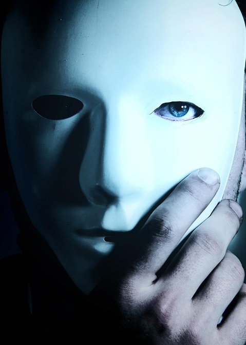 Uma pessoa de olhos azuis segura uma máscara branca sobre o seu rosto.
