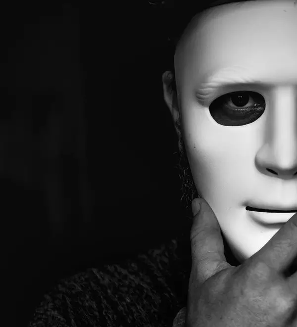 Uma pessoa em um ambiente escuro segura uma máscara branca na frente do rosto