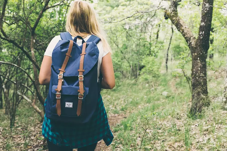 Adolescente com mochila nas costas andando em uma área verde.
