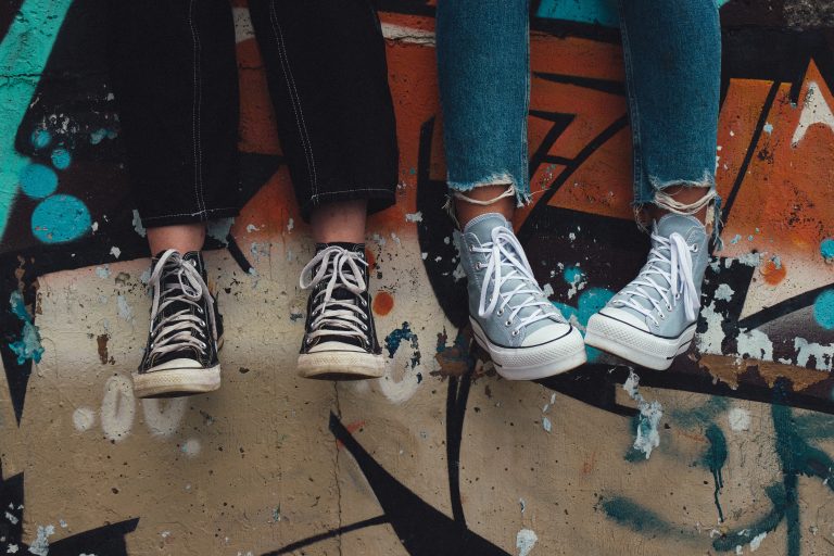 quatro pernas e pés encostados em uma parede colorida grafitada, todos com calças jeans e all star: capa do conteúdo de comportamentos típicos da adolescência