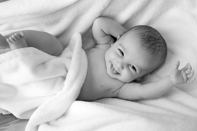 Bebê sorrindo envolto em lençóis em preto e branco